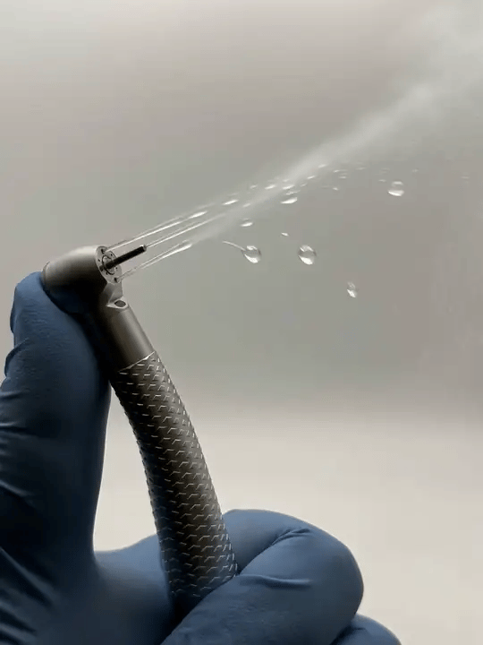 A gloved hand holding the handpiece while a fine water spray leaves the head